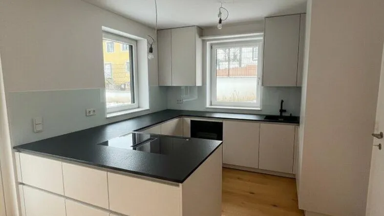 Moderne Küche mit U-förmiger Arbeitsplatte, dunkler Oberfläche und hellem Holzfußboden.
