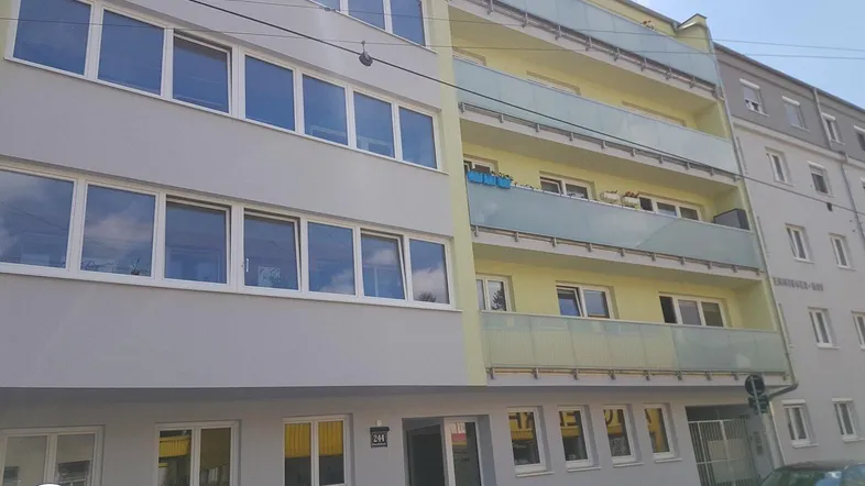 Mehrstöckiges Wohngebäude mit hellgelber und grauer Fassade sowie mehreren Balkonen.