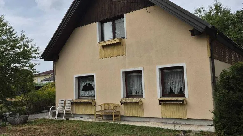 Ansicht des Hauses von der Seite mit Gartenbereich, Rasenfläche und einfacher Sitzgelegenheit im Freien.