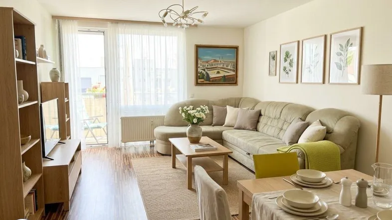Helles Wohn- und Esszimmer mit beigem Ecksofa, Holzboden und Zugang zum Balkon.
