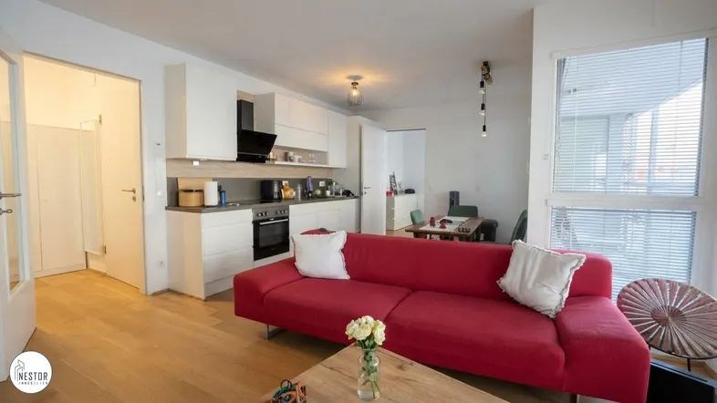 Heller offener Wohnbereich mit rotem Sofa, integrierter Küche und Essbereich, ausgestattet mit Holzfußboden.