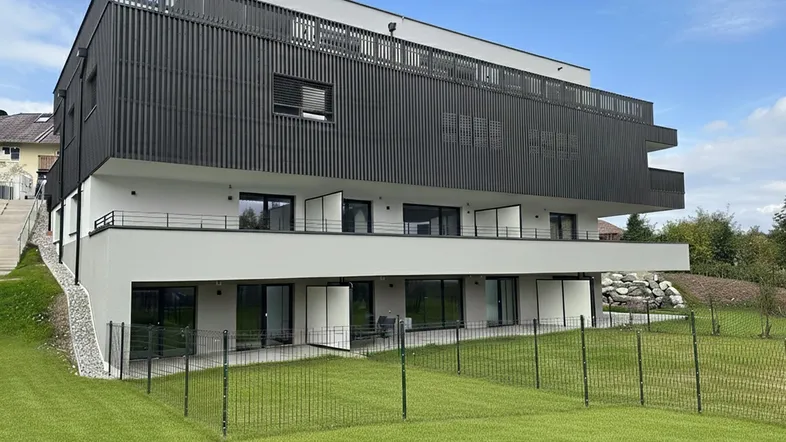 Modernes Mehrfamilienhaus mit klarer Architektur, Balkonen, Terrassen und gepflegter Rasenfläche in grüner Umgebung.