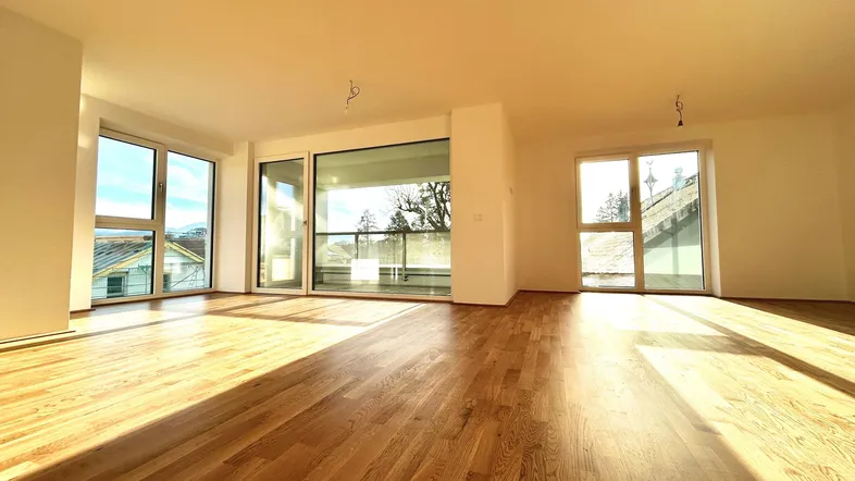 Heller Wohnraum mit Holzboden und großen Fenstern, die viel Tageslicht hereinlassen.