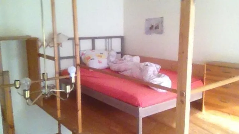 Schlafbereich auf einer Holzkonstruktion mit Bett und einfacher Beleuchtung in einem hellen Raum.