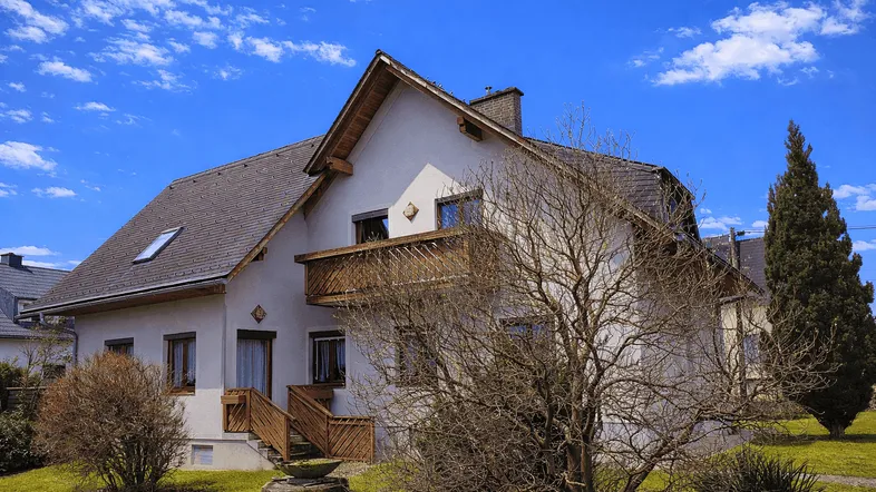 Charmantes Einfamilienhaus mit Balkon und Satteldach unter blauem Himmel.