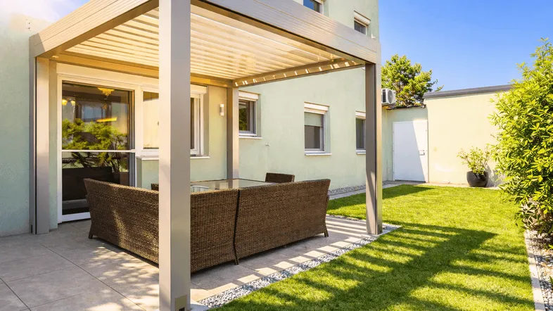 Moderne Terrasse mit Pergola und bequemen Loungemöbeln, umgeben von einem gepflegten Rasen.