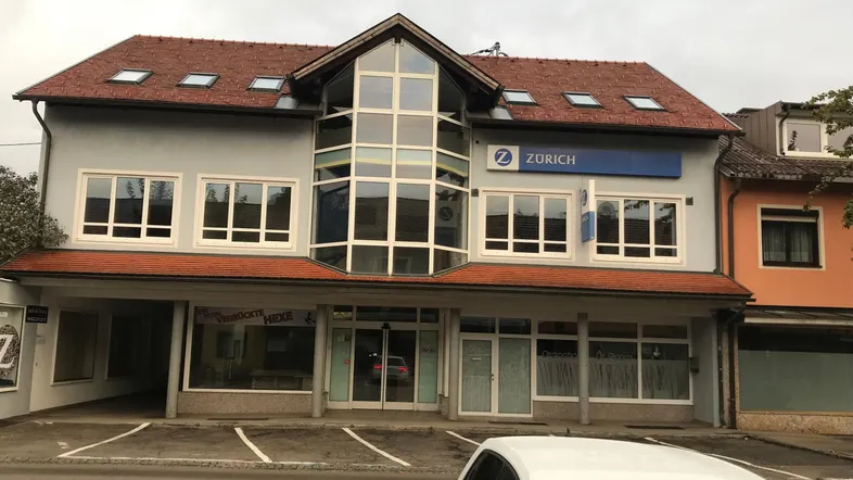 Gebäudeansicht mit moderner Glasfassade im Eingangsbereich und Geschäftsräumen im Erdgeschoss.