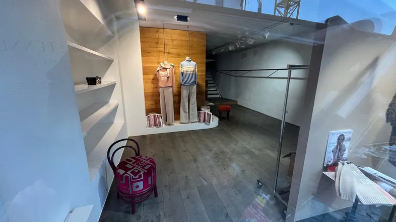 Schaufensteransicht eines Ladenlokals mit Holzboden, Regalen und Schaufensterpuppen, teilweise reflektiert.