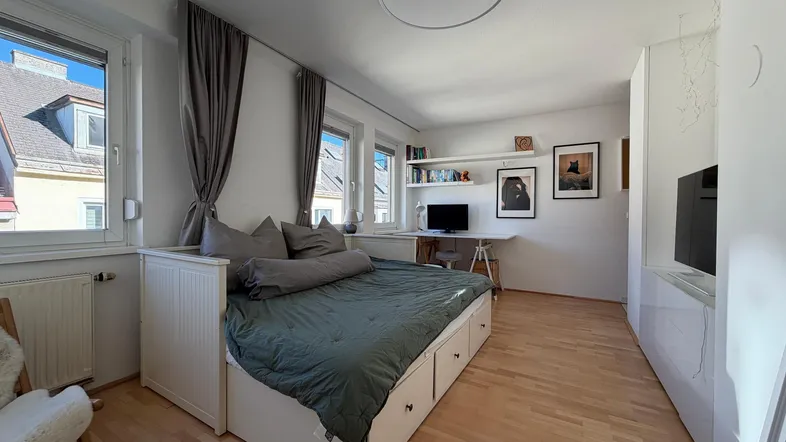 Helles Schlafzimmer mit Holzboden, einem Bett mit Stauraum und einem Arbeitsbereich am Fenster.