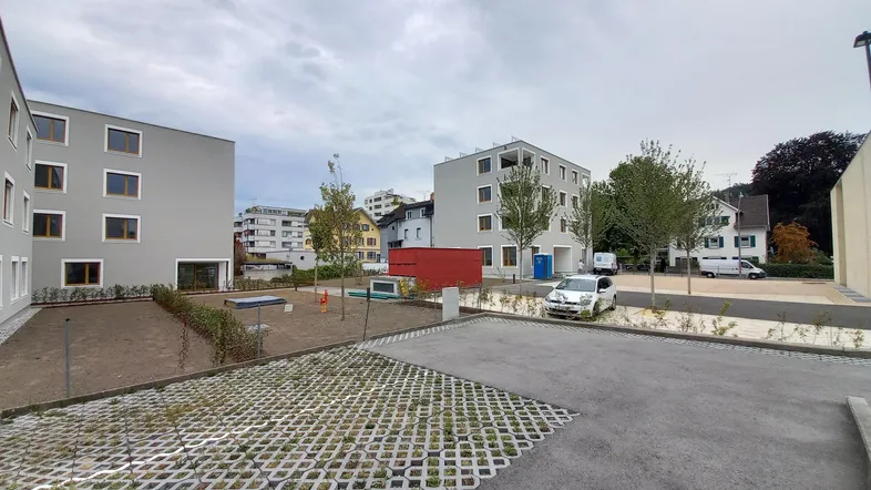 Moderne Wohngebäude mit schlichter Fassade und Außenparkplätzen in einer städtischen Umgebung unter bewölktem Himmel.