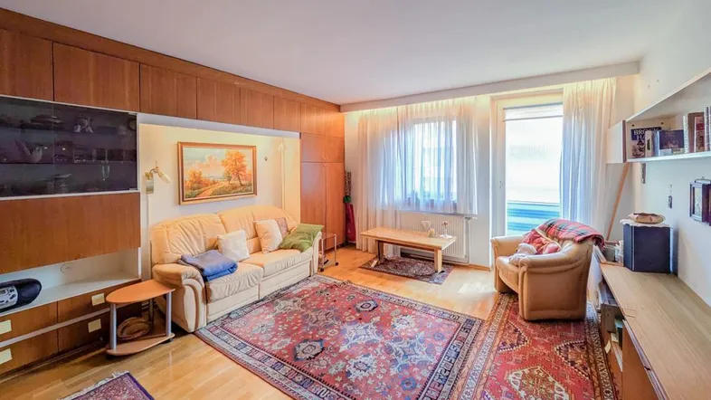 Gemütliches Wohnzimmer mit Holzvertäfelung, Teppichboden und großem Fenster, das viel Licht hereinlässt.