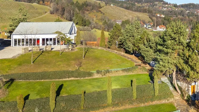 Modernes Gebäude mit großen Glasfronten, umgeben von terrassierten Rasenflächen und einer hügeligen Landschaft.