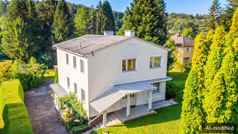 Weißes Einfamilienhaus mit Satteldach, umgeben von viel Grün und Bäumen in ländlicher Umgebung.