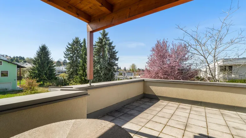 Geräumige Terrasse mit Fliesenboden und Holzdach, bietet einen weiten Blick ins Grüne.
