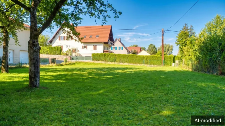 Gepflegte Rasenfläche mit Baum und Hecke, umgeben von Wohnhäusern in ländlicher Umgebung.