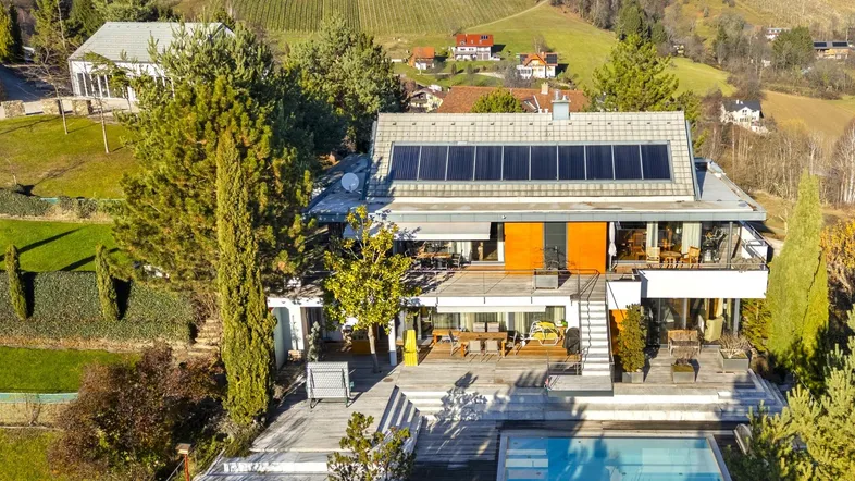 Moderne Villa mit Solaranlage, Pool und weitläufigem Garten in hügeliger Landschaft.