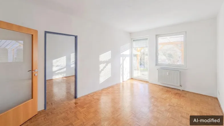 Helles Zimmer mit Parkettboden und großen Fenstern, das viel Tageslicht hereinlässt.