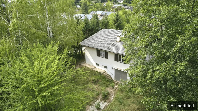 Luftaufnahme eines Einfamilienhauses mit grauem Dach, umgeben von üppigem Grün und Bäumen.