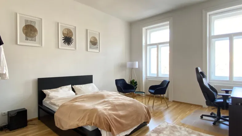 Helles Schlafzimmer mit Holzboden, Doppelbett, Schreibtisch und zwei großen Fenstern.