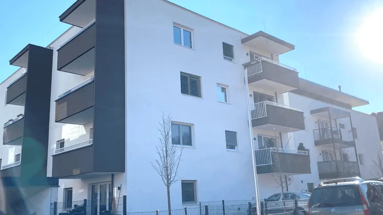 Modernes Mehrfamilienhaus mit weißer Fassade und dunklen Balkonen unter blauem Himmel.