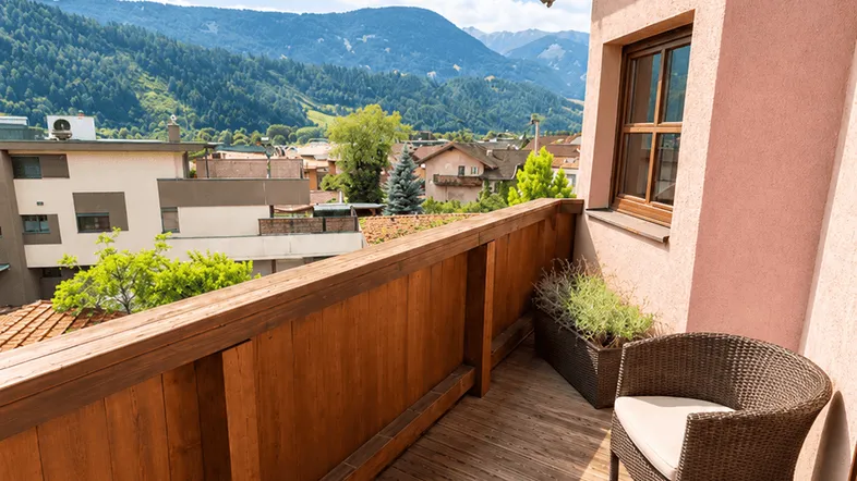 Sonniger Balkon mit Holzboden und Rattanmöbeln bietet einen weiten Blick auf die Berge.