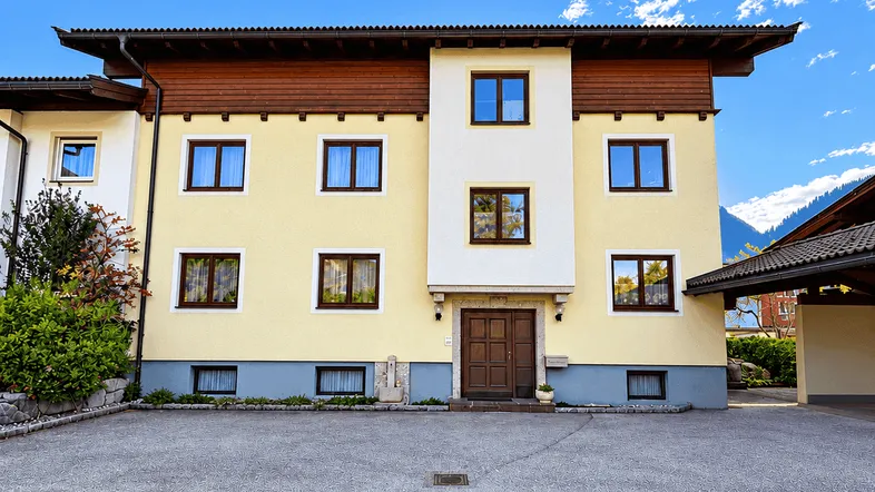 Gepflegtes Mehrfamilienhaus mit traditioneller Architektur, gelber Fassade und braunen Fensterrahmen unter blauem Himmel.