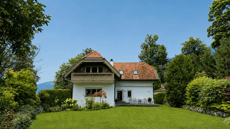 Freistehendes Haus mit rotem Ziegeldach und großem, gepflegten Garten unter blauem Himmel.