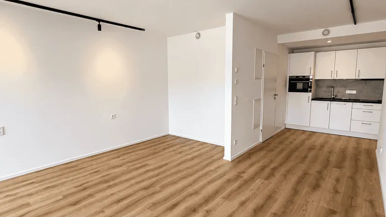Heller offener Wohnbereich mit integrierter Küchenzeile und modernem Laminatboden.