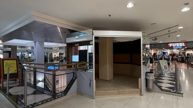 Leerer Verkaufsstand in einem Einkaufszentrum mit Fliesenboden und Blick auf die umliegenden Geschäfte.