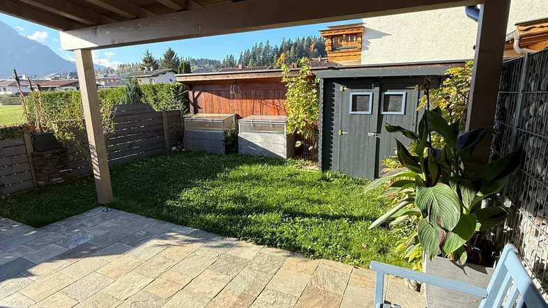 Überdachte Terrasse mit Fliesenboden, Sitzbank und Blick auf den Garten sowie die umliegenden Berge.