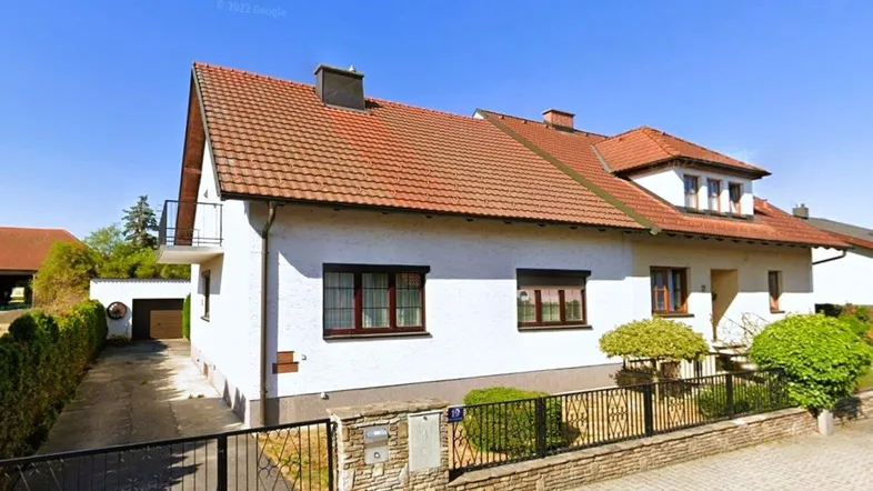 Gut gepflegtes Einfamilienhaus mit weißer Fassade, rotem Satteldach, Balkon und Garage.