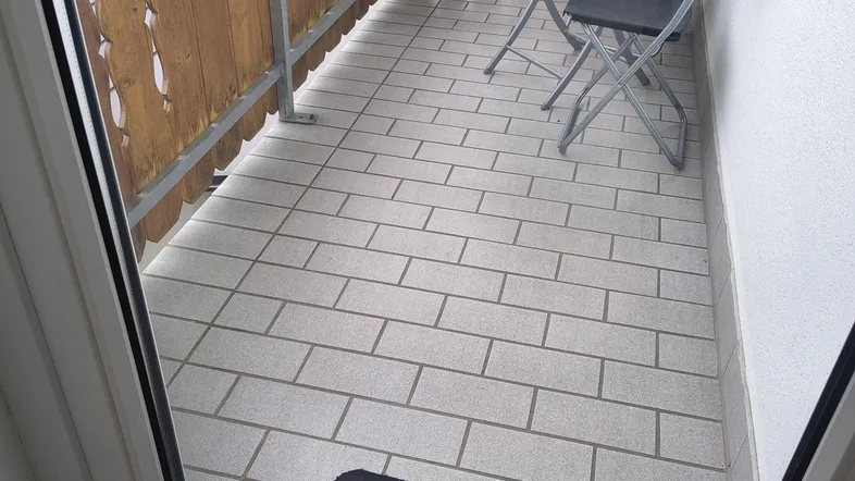 Kleiner Balkon mit Fliesenboden und Holzgeländer, möbliert mit Tisch und Stühlen.