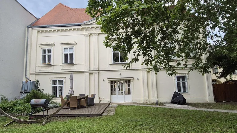 Großer Gartenbereich mit Holzterrasse, Grill und Sitzgelegenheiten vor der historischen Fassade.