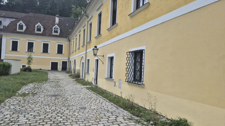 Kopfsteinpflasterweg führt entlang der gelben Fassade eines historischen Gebäudes mit schmiedeeisernen Fenstergittern.