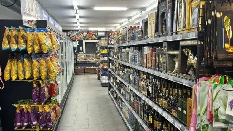 Langer Gang eines Einzelhandelsgeschäfts mit Regalen voller Produkte und Flaschen unter Leuchtstofflampen.
