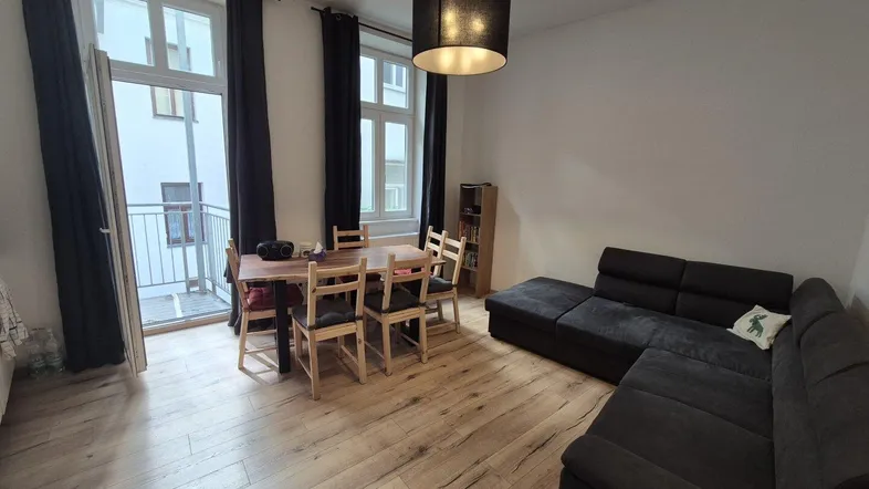 Heller Wohn- und Essbereich mit Holzboden, großem Sofa und Zugang zu einem kleinen Balkon.