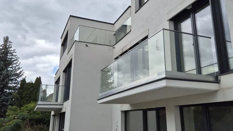 Moderne Wohnanlage mit mehreren Balkonen und Glasgeländern unter bewölktem Himmel.