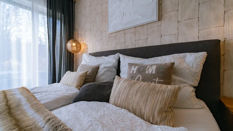 Gemütliches Schlafzimmer mit strukturierten Tapeten, großem Bett und dekorativer Beleuchtung.
