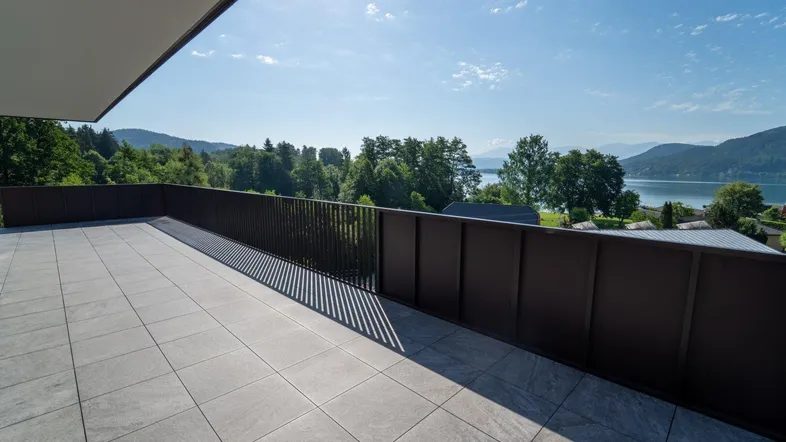 Große geflieste Terrasse mit Seeblick und moderner Brüstung unter blauem Himmel.
