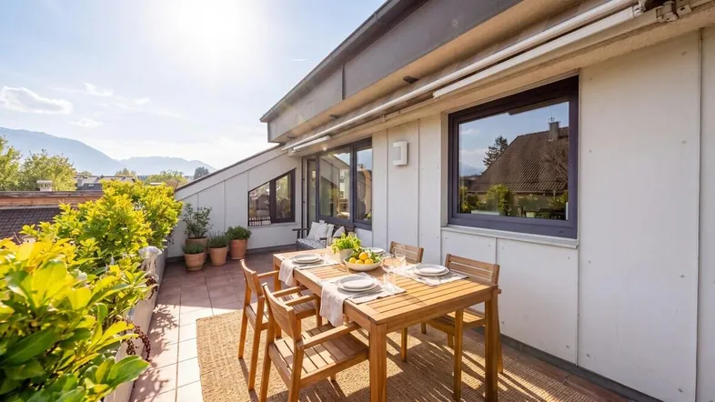 Sonnige Dachterrasse mit Esstisch, Pflanzen und weitem Blick auf die Umgebung und Berge.