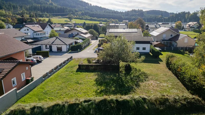Luftaufnahme eines unbebauten Grundstücks in einer Wohngegend mit umliegenden Häusern und Bergen.