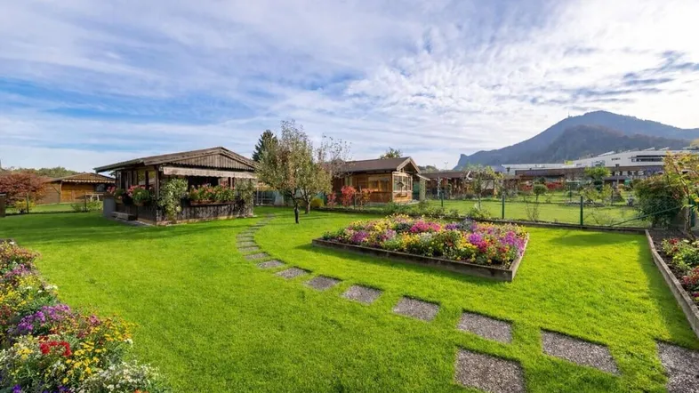 Weitläufiger Garten mit bunten Blumenbeeten, Steinpfad und Blick auf die umliegenden Berge.