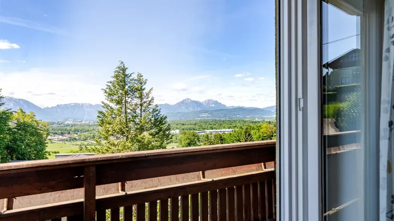 Blick vom Balkon auf die weite Landschaft mit Bergen und grünen Bäumen unter blauem Himmel.
