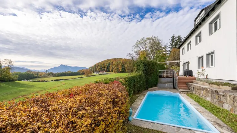 Außenansicht des Hauses mit Pool, umgeben von grünen Wiesen und herbstlichen Bäumen mit Bergblick.