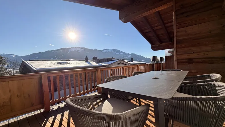 Sonniger Balkon mit Holzboden, modernen Outdoor-Möbeln und herrlichem Bergblick.