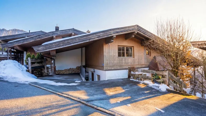 Charmantes Holzhaus im alpinen Stil mit verschneiter Zufahrt an einem sonnigen Wintertag.