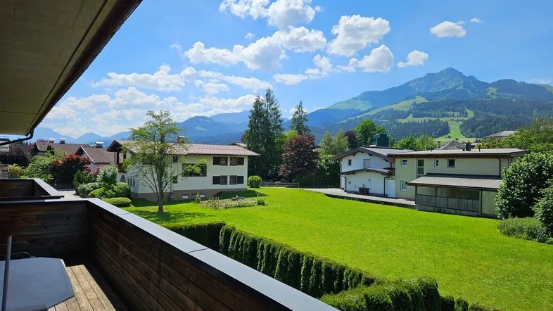 Geräumiger Balkon mit Holzboden und weitem Blick auf grüne Wiesen und die umliegende Berglandschaft.