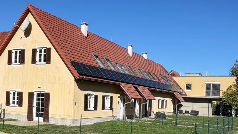 Gelbes Haus mit rotem Ziegeldach, Solarpaneelen und großem Gartenbereich unter blauem Himmel.