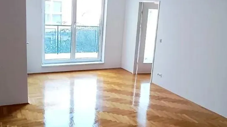 Geräumiges Zimmer mit glänzendem Fischgrätparkett und großen Fenstern, die viel Tageslicht hereinlassen.