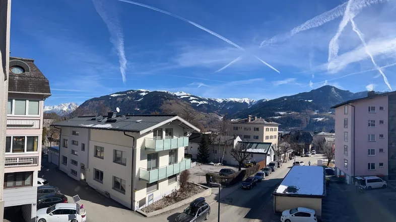 Weitläufiger Blick über die Stadt mit schneebedeckten Bergen im Hintergrund unter strahlend blauem Himmel.